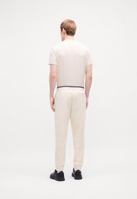 Cremefarbendes T-Shirt und passende Hose mit einem schwarz gestreiften Bündchen. Das Outfit hat eine glatte Textur und einen lässigen Schnitt.