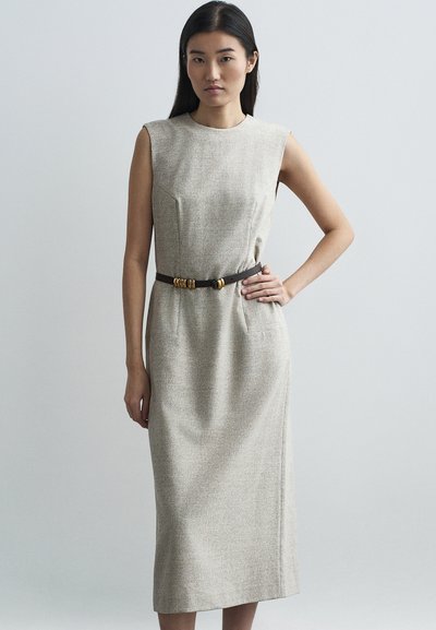 Robe cintrée beige avec un décolleté rond, des manches courtes et une silhouette ajustée. Elle présente une ceinture marron avec des accents métalliques et des poches latérales.