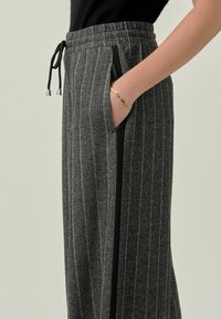 Grau gestreifte, weit geschnittene Hose aus weichem Stoff, mit einem schwarzen Seitenpanel, kontrastierendem Kordelzug und Seitentaschen.
