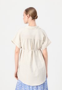 Camicia a righe chiare in beige e crema con vita arricciata, maniche corte e orlo curvo, vista da dietro.