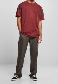 Camiseta de algodón color granate con detalles grises en los hombros, combinada con pantalones grises de corte holgado y zapatillas negras con suelas blancas.