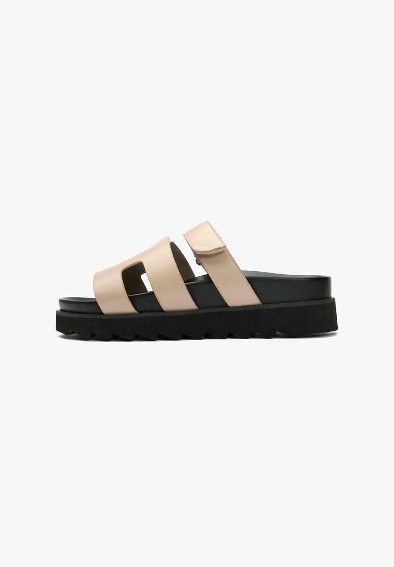 Beige slide sandal with two wide straps and Velcro closure, constructed from smooth material. Black platform sole with a jagged edge.
