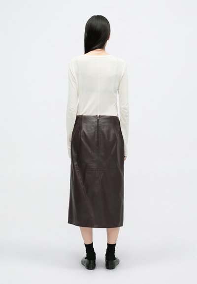 Blusa de manga larga en color crema, con un corte relajado, combinada con una falda midi de cuero marrón oscuro que presenta un cierre en la parte posterior. Color sólido, textura suave.