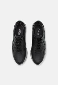 Black leather sneakers with textured surface, featuring round toe, lace-up front, and subtle green accents on the sides.