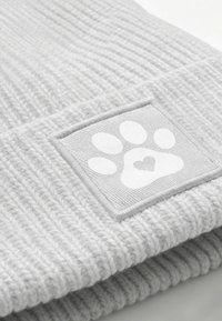 Gray knitted beanie with a textured surface, featuring a square patch with a white paw print and heart design.