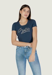 Maglietta a maniche corte color blu navy con logo "Guess" decorato in argento, design aderente con scollatura a girocollo e tessuto morbido.