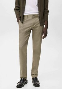 Kakhi chinos i bomullsblandning med rak bendesign, sidofickor och bakfickor, samt en klassisk knappstängning, kombinerat med svarta loafers.
