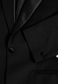 Chaqueta de traje negra con tejido liso, con solapa con muesca, cierre de un solo botón y bolsillo de ojal. Diseño texturizado y entallado.