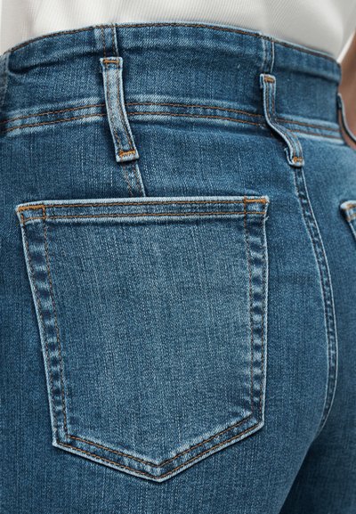 Κοντινή λήψη μπλε τζιν τζιν με πίσω τσέπη, θηλιές για ζώνη και πορτοκαλί ραφές στη μέση και τις ραφές.