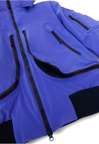 Lila vízálló dzseki fekete cipzárakkal, több cipzáras zsebbel és bordázott mandzsettákkal. Simább textúra, modern design és karcsú fazon.