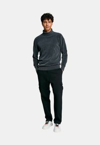 Maglione grigio a collo alto, morbido al tatto, dalla vestibilità rilassata. Abbinato a pantaloni neri con tasche cargo e sneakers bianche con lacci colorati.