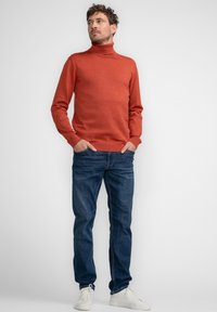 Orange Rollkragenpullover aus glattem Material, kombiniert mit blauen Jeans und weißen Sneakern. Einfaches Design, keine sichtbaren Muster.