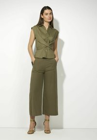 Olijfgroene, korte mouwen shirt met een knoopdesign in de taille, gecombineerd met een wijde broek. Sandalen met open tenen en groene hoge hakken maken de look compleet.