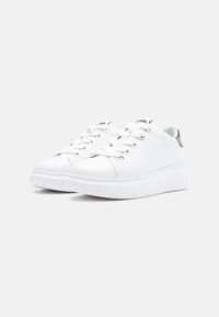 Beli supergi z gladkim usnjem zgoraj, okroglo konico, ravnimi vezalkami in debelim podplatom. Na peti ima kovinski dodatek za večji poudarek.