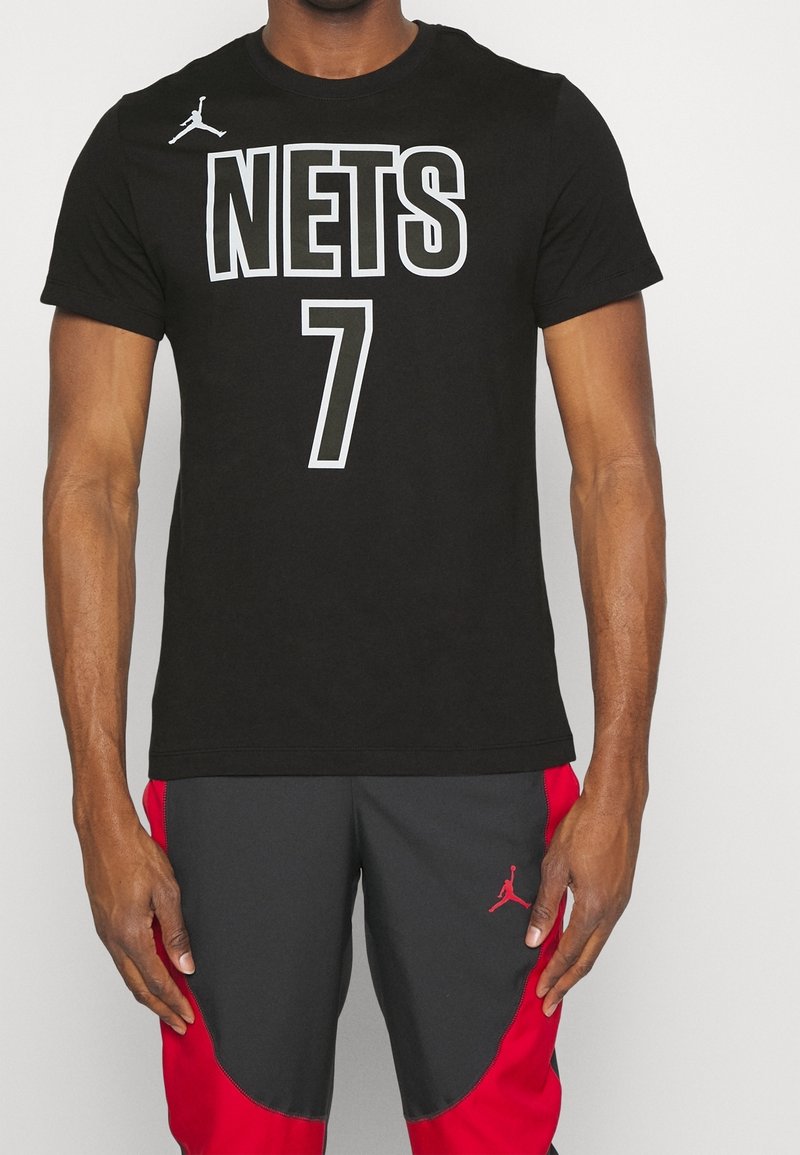 Mustapainen puuvillapaita, jossa on rohkealla valkoisella fontilla "NETS" ja "7", sekä pieni valkoinen Jumpman-logo vasemmassa olkapäässä.