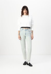 Sweatshirt branco curto com uma faixa elástica preta, combinado com jeans de cintura alta de tom azul claro e mocassins pretos. Tecido suave, ajuste casual.