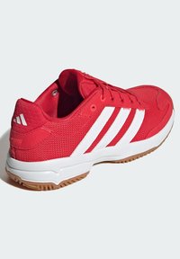 Baskets de sport rouges en mesh et matériau synthétique, avec des rayures blanches, un col rembourré et une semelle en caoutchouc naturel.