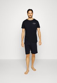 Donkerblauwe katoenen T-shirt voor heren met korte mouwen en logo op de borst, gecombineerd met bijpassende knielange shorts, beide met een gladde textuur.
