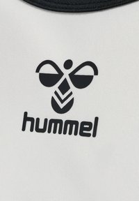 Logo d’abeille stylisée noire au-dessus du mot « hummel » sur tissu blanc avec un bord de col noir visible en haut.