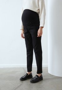 Svarta gravidjeans med en stretchig svart panel, slim fit och framfickor, ihop med platta svarta skor och en krämfärgad tröja.