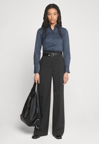 Camicia blu navy con maniche lunghe, abbinata a pantaloni neri a vita alta e a gamba larga. Borsa in pelle nera con un design morbido.