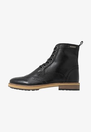 Bottine brogue en cuir noir avec lacets à l'avant, détails perforés, semelle beige et talon empilé.