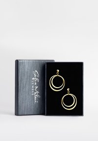 Orecchini a cerchio in oro con due design circolari intrecciati, esposti in una scatola regalo foderata di velluto nero con un logo argento sul coperchio.