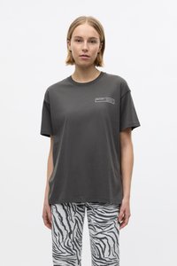 Charcoal gray cotton t-shirt with short sleeves and round neck; features a white rectangular label on the left chest. Paired with zebra-patterned pants.