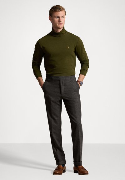 Olive zaļš turtlenecks džemperis saskaņots ar pelēkiem piegriezuma biksēm. Brūnas ādas mokasīni un pulkstenis izceļ apģērba detaļas.