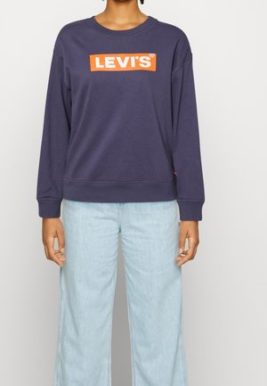 Mörkblå Levi's sweatshirt med orange logotyp, rund halsringning, långa ärmar och ribbade muddar, ihop med ljusblå vida jeans.