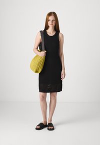 Vestido preto sem mangas com um padrão texturizado, combinado com uma mala amarela descontraída e sandálias pretas deslizantes. Design simples e moderno.