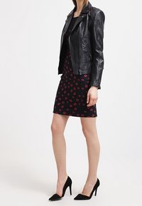 Veste de moto en cuir noir sur une robe noire ajustée avec imprimé de lèvres rouges ; associée à des chaussures à talons hauts noires. Textures lisses et design épuré.