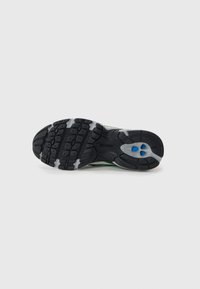 Semelle de chaussure de sport noire en caoutchouc texturé pour une adhérence, avec une semelle intermédiaire grise et des accents bleus près du talon pour la stabilité.