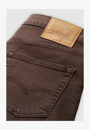 Kastanjebruine spijkerbroek van denim met een leren label met reliëftekst, een achterzak met een kenmerkend stikpatroon en een gladde textuur.