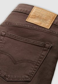 Bruna jeans i denim med en läderlapp med präglad märkning, bakficka med signaturstygn och en slät, texturerad yta.