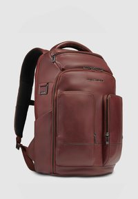 Mochila de cuero marrón con correas ajustables, múltiples compartimentos con cremallera, acabado texturizado y elegantes detalles metálicos.