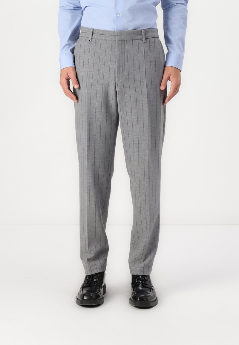 Pantalones gris claro a rayas con un corte recto, con una textura suave y pliegues frontales, combinados con zapatos negros de cordones.