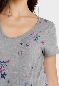 Camiseta gris de manga corta con escote redondeado, que presenta un patrón de estrellas multicolores en rosa, azul y morado sobre la tela.