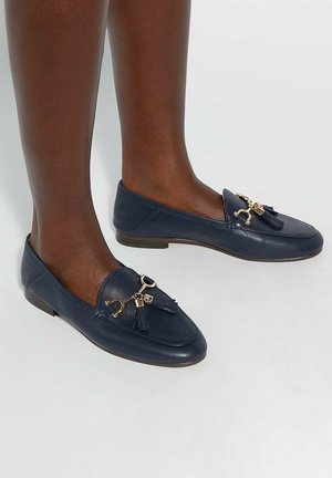 Navy blue leather loafers featuring a gold-tone hardware accent with tassels and a flat sole. Smooth texture with minimal stitching details.