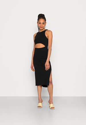 Vestido preto sem mangas com recorte na cintura, comprimento midi, fenda lateral e tecido suave. Combinado com mules de salto bloco amarelo claro.