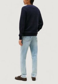 Marinblå stickad tröja med ribbade ärmslut, i kombination med ljusblå raka jeans och mörkbruna loafers, sedd bakifrån.