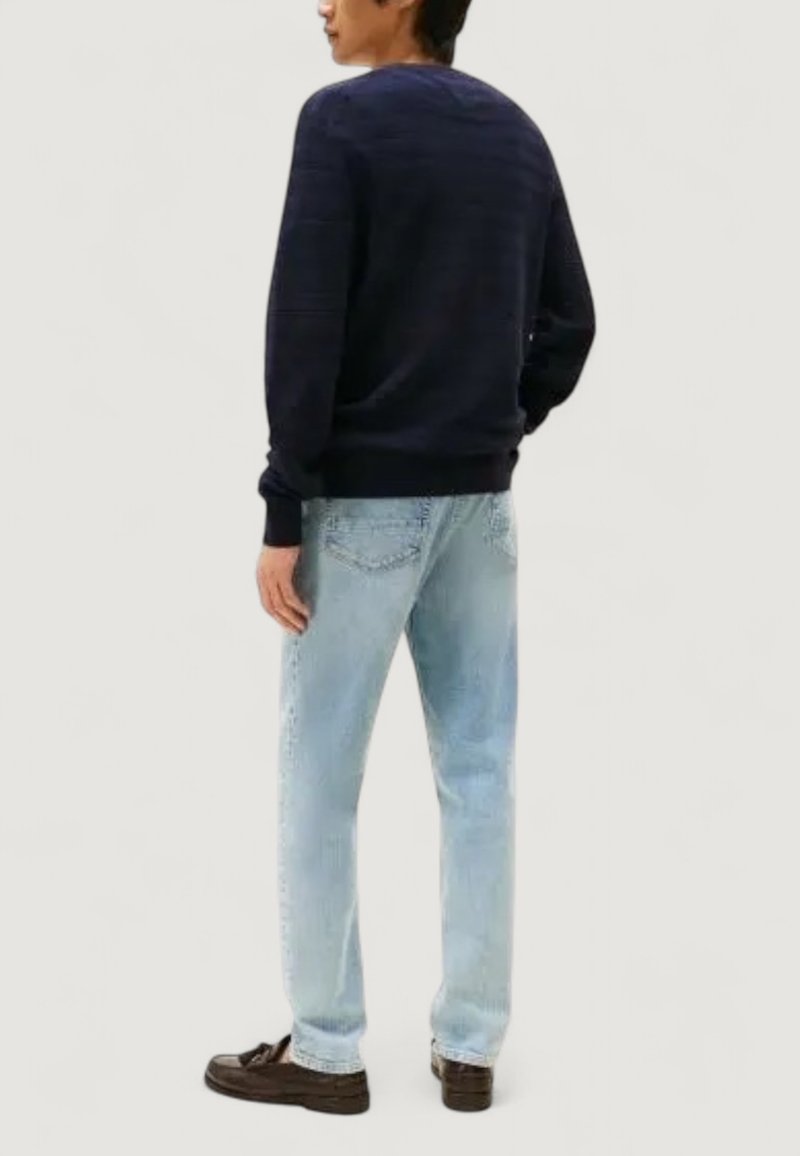 Marinblå stickad tröja med ribbade ärmslut, i kombination med ljusblå raka jeans och mörkbruna loafers, sedd bakifrån.