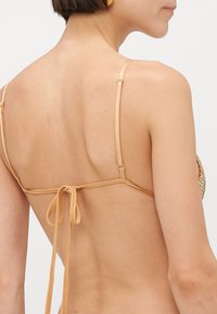Achteraanzicht van een tan bikini-top met dunne verstelbare banden, een striksluiting aan de achterkant en gouden hardware-details. Geweven stof met een subtiele glans.