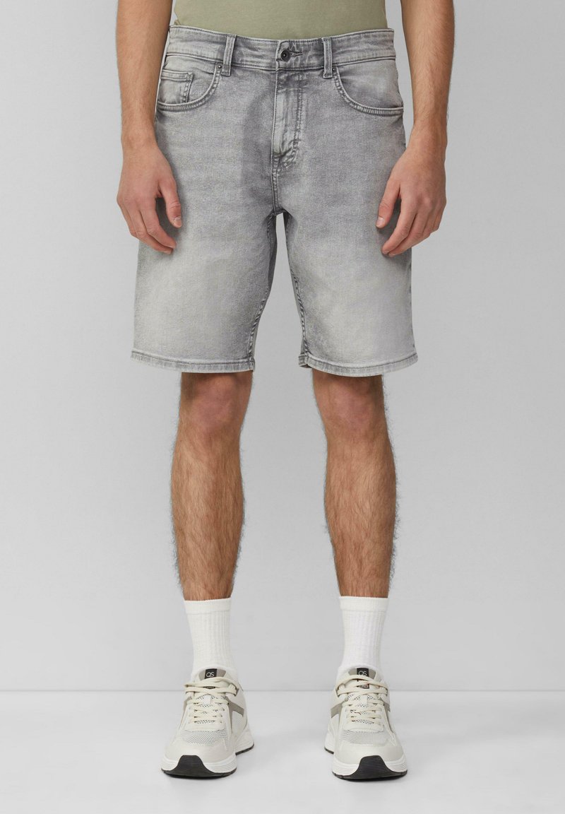 Szare szorty dżinsowe z wyblakłym wzorem, pięć kieszeni i proste dopasowanie. Noszone z białymi skarpetami i beżowymi trampkami.