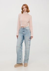 Maglione corto a collo alto lavorato a maglia di colore rosa chiaro abbinato a jeans cargo oversize di colore blu chiaro con tasche laterali e un lavaggio sbiadito.