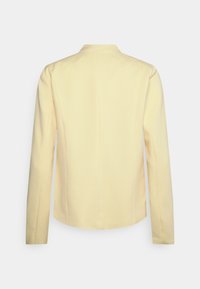 Vaaleankeltainen räätälöity jakku, jossa on pitkät hihat, sileä pinta ja hienovarainen ribbineuloskuvio, ja jossa on lovikaulus sekä rakenteellinen istuvuus.