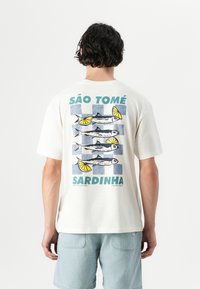 White cotton t-shirt featuring a graphic print of sardines and lemons in blue and green, with "SÃO TOMÉ" and "SARDINHA" text.