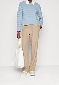 Maglione a righe blu chiaro con colletto bianco, pantaloni beige con vita elastica e borsa in tessuto bianca. Sneakers neutre.