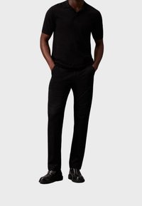 Zwarte polo met korte mouwen, gecombineerd met zwarte op maat gemaakte broek. Zwarte veterschoenen maken de outfit compleet. Eenvoudig ontwerp en effen kleur.