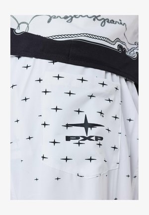 Witte shirt met zwart kruispatroon, voorzien van een zak en zwarte tailleband. Inclusief "PXP" logo gedrukt op de zak.